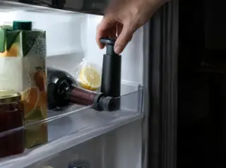Gros plan sur une bouteille rebouchée couchée dans la porte d'un frigo, une pompe à vide posée sur l'étagère