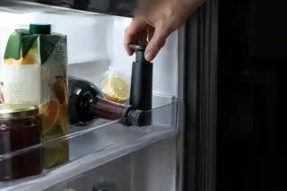 Gros plan sur une bouteille rebouchée couchée dans la porte d'un frigo, une pompe à vide posée sur l'étagère