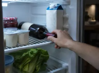 Gros plan sur une main qui prend une bouteille de vin rouge couchée dans un frigo entre les yaourts et le lait