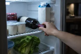 Gros plan sur une main qui prend une bouteille de vin rouge couchée dans un frigo entre les yaourts et le lait
