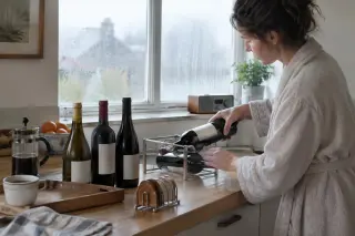 Une femme couche une bouteille dans un porte-bouteille sur un plan de travail où d'autres sont debout près d'un plateau