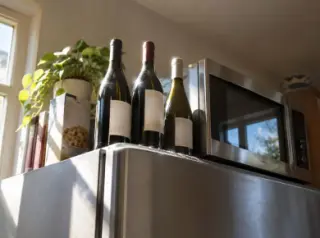 Vu d'en bas, des bouteilles de vin debout sur un frigo à côté du micro-ondes, en plein soleil de cuisine
