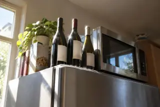 Vu d'en bas, des bouteilles de vin debout sur un frigo à côté du micro-ondes, en plein soleil de cuisine