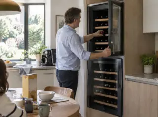 Un homme ouvre la porte haute d'une cave à vin encastrée en colonne à deux portes dans sa cuisine, le matin