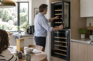 Un homme ouvre la porte haute d'une cave à vin encastrée en colonne à deux portes dans sa cuisine, le matin
