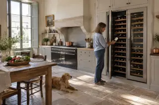 Une femme sort une bouteille d'une double colonne de cave à vin encastrée dans une cuisine de grande maison ancienne rénovée