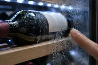 Gros plan sur des gouttes de condensation sur une bouteille et la vitre intérieure d'une cave, un doigt les essuie