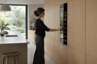 Dans une cuisine d'architecte sans poignées, une femme ouvre par pression une cave à vin affleurante dans le mur de placards