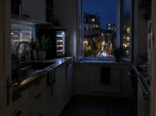 Une cuisine étroite la nuit, la cave à vin allumée, la fenêtre ouverte sur les lumières de la ville