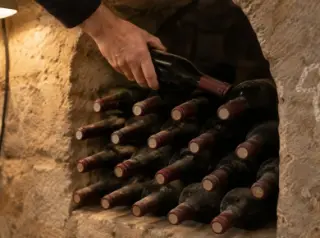 Gros plan sur des bouteilles empilées en quinconce dans une alvéole de pierre, une main en pose une de plus
