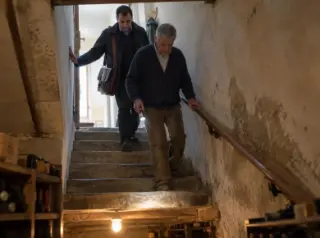 Un agent d'assurance à sacoche descend l'escalier d'une cave avec le propriétaire qui éclaire les marches à la lampe