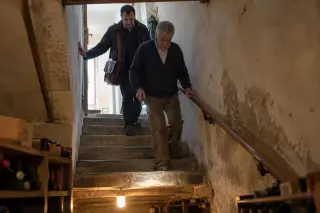 Un agent d'assurance à sacoche descend l'escalier d'une cave avec le propriétaire qui éclaire les marches à la lampe