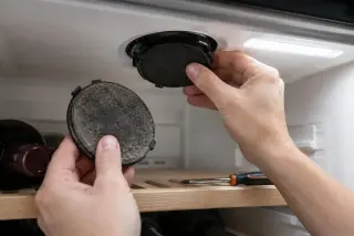 Gros plan sur des mains remplaçant le petit filtre à charbon rond au plafond d'une cave à vin, l'ancien filtre noirci