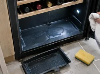Vue de dessus du fond d'une cave à vin avec une petite flaque d'eau, le bac de récupération sorti et une éponge