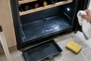 Vue de dessus du fond d'une cave à vin avec une petite flaque d'eau, le bac de récupération sorti et une éponge