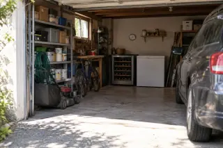 Une cave à vin dans un coin de garage encombré, thermomètre mural à aiguille, une voiture, la porte ouverte sur l'été