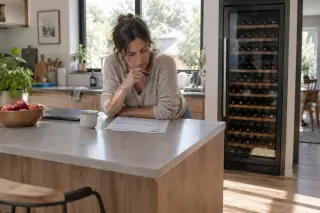 Une femme lit une facture posée sur l'îlot de sa cuisine, une grande cave à vin à côté de l'îlot