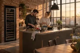 Un couple cuisine dans la cuisine ouverte d'un loft à l'heure dorée, une grande cave à vin à deux zones contre le mur de briques