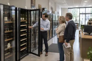 Dans un magasin spécialisé, un vendeur ouvre la porte d'une grande cave à vin devant un couple, rangée de grandes caves