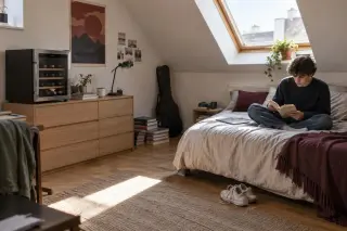 Une petite cave à vin de vingt bouteilles posée sur un meuble bas dans une chambre mansardée d'étudiant, sous le Velux
