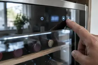 Gros plan sur un index qui presse une touche tactile du bandeau d'une cave à vin, chiffres illisibles