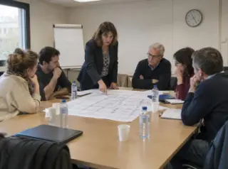 Réunion de copropriétaires autour d'une table, un plan de sous-sol déplié, le syndic debout