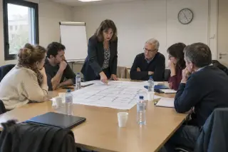 Réunion de copropriétaires autour d'une table, un plan de sous-sol déplié, le syndic debout