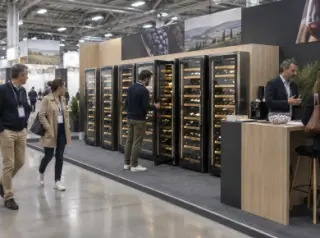 Dans une halle d'exposition, des armoires de vieillissement alignées sur un stand, des visiteurs à badges passent