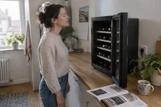 Une femme ferme les yeux devant la porte ouverte de sa cave à vin pour sentir le froid, brochure aux prix flous sur le plan