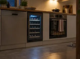 Une cave à vin encastrée sous le plan de travail entre le lave-vaisselle et le four, plinthes, lumière de la hotte