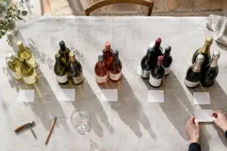 Vue de dessus de bouteilles groupées par famille sur une nappe de lin, un carré de papier blanc devant chaque groupe