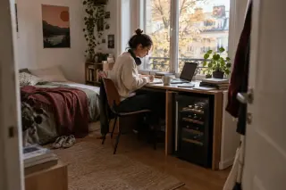 Une étudiante révise à son bureau dans son studio, une petite cave à vin logée sous le bureau, après-midi d'automne