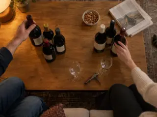 Vue de dessus d'une table basse où un couple a séparé les bouteilles à boire et à garder, ils en choisissent une pour le dîner