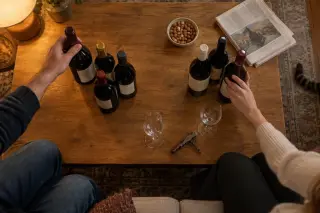 Vue de dessus d'une table basse où un couple a séparé les bouteilles à boire et à garder, ils en choisissent une pour le dîner