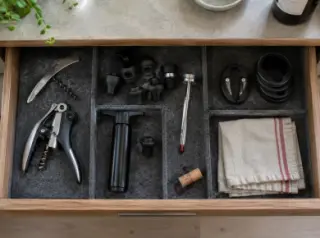 Vue de dessus d'un tiroir de cuisine ouvert : tire-bouchons, bouchons hermétiques, pompe à vide, thermomètre, collerettes