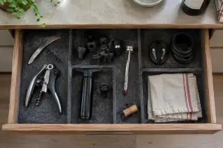 Vue de dessus d'un tiroir de cuisine ouvert : tire-bouchons, bouchons hermétiques, pompe à vide, thermomètre, collerettes
