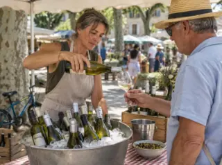 Une vigneronne sert un verre de vin blanc à un client sur un marché de producteurs en plein été