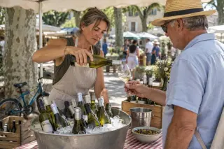 Une vigneronne sert un verre de vin blanc à un client sur un marché de producteurs en plein été
