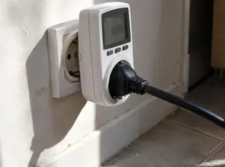 Gros plan sur un wattmètre de prise branché au mur, le câble d'une cave à vin part hors champ