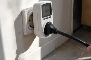 Gros plan sur un wattmètre de prise branché au mur, le câble d'une cave à vin part hors champ