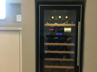 Wall niche with compact built-in wine fridge, bottles on wooden racks, modern kitchen background, natural light