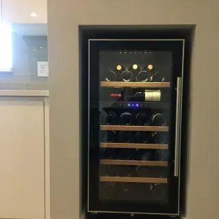 Wall niche with compact built-in wine fridge, bottles on wooden racks, modern kitchen background, natural light