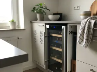 Freestanding wine fridge partly enclosed under a kitchen counter in a modern kitchen, with wine bottles visible inside.