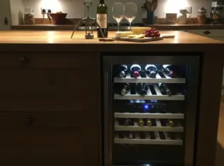 Kitchen island with built-in wine fridge, wine bottles visible inside, open wine and glasses on countertop in a warmly lit, inviting kitchen