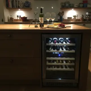 Kitchen island with built-in wine fridge, wine bottles visible inside, open wine and glasses on countertop in a warmly lit, inviting kitchen