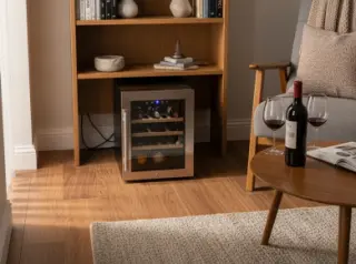 Electric wine fridge in a cozy living room corner on a rug, next to bookshelf and armchair, with bottles and glasses, in natural daylight