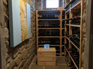 Cozy amateur photo of an insulated rustic wine cellar with wine racks, insulation on one wall, a digital hygrometer, and soft natural light.