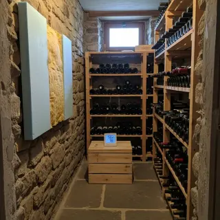 Cozy amateur photo of an insulated rustic wine cellar with wine racks, insulation on one wall, a digital hygrometer, and soft natural light.