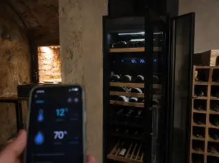 Connected electric wine cellar with digital display, open door showing bottles, smartphone app controlling temperature and humidity, modern home interior.