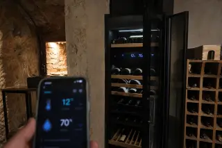 Connected electric wine cellar with digital display, open door showing bottles, smartphone app controlling temperature and humidity, modern home interior.